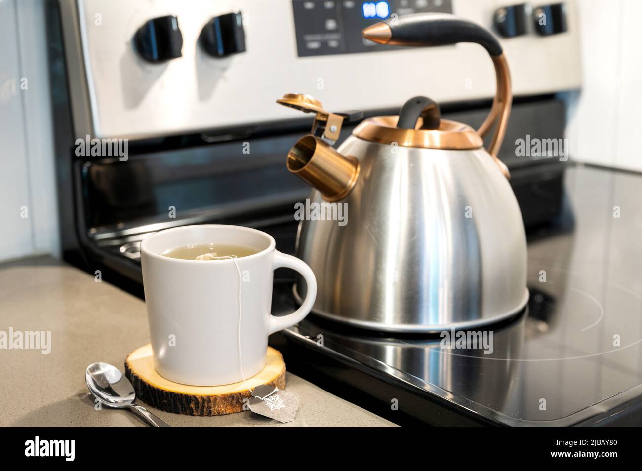 A mug of tea or coffee on a wooden cutting board with a kettle in the background. Stock Photo