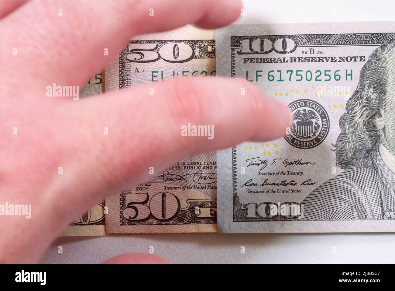 Close-up of a human left hand reaching for a small pile of United States currency banknotes on a white surface table. Stock Photo