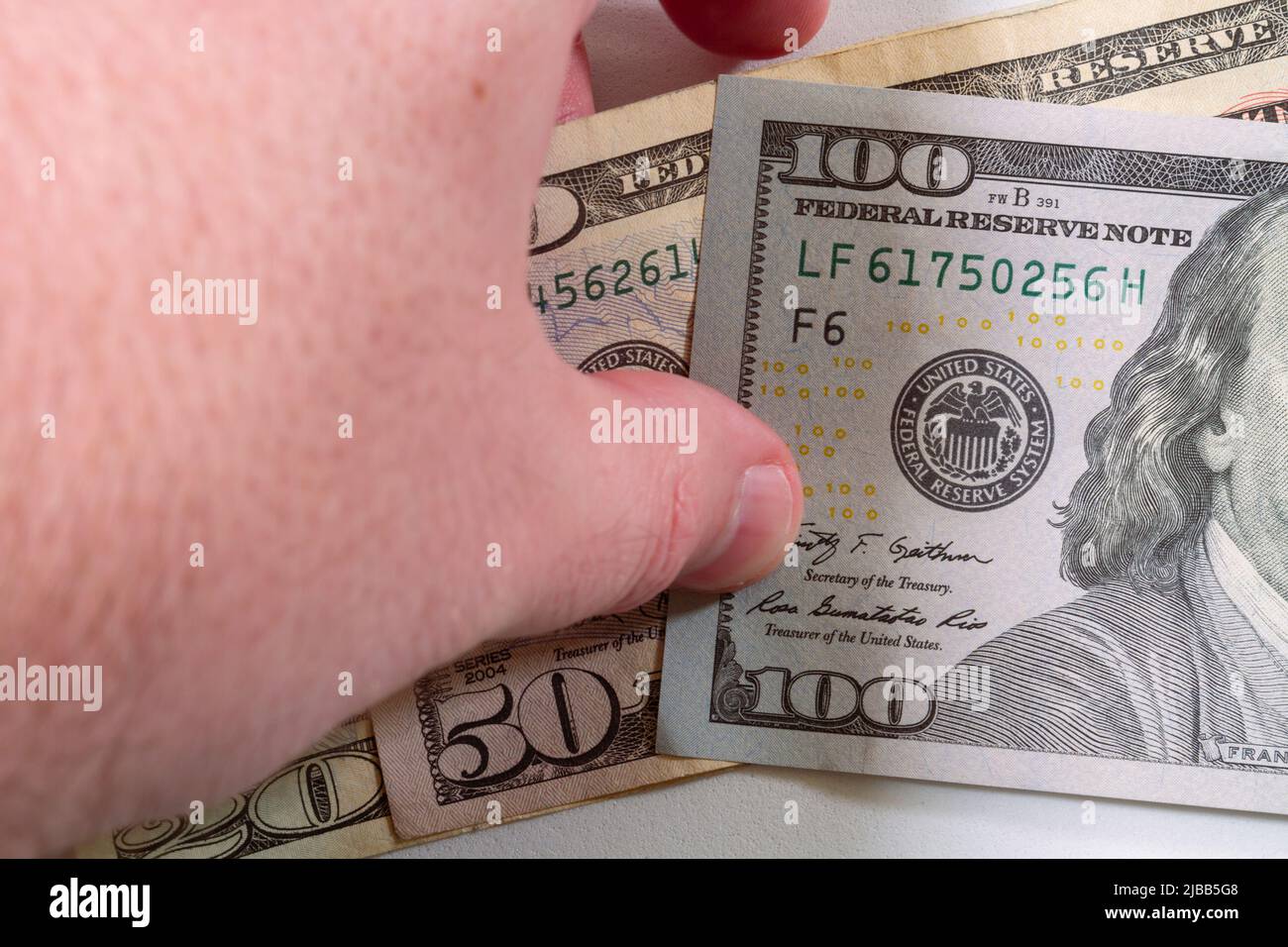 Close-up of a human left hand picking up a small pile of United States currency banknotes on a white surface table. Stock Photo