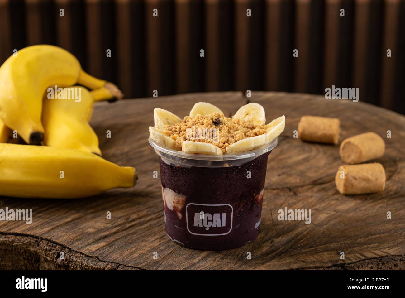 Delicious Brazilian Açaí Cream, in a plastic Cup With banana and ground peanuts Topping, in a rustic wooden background. Summer acai smoothie Stock Photo