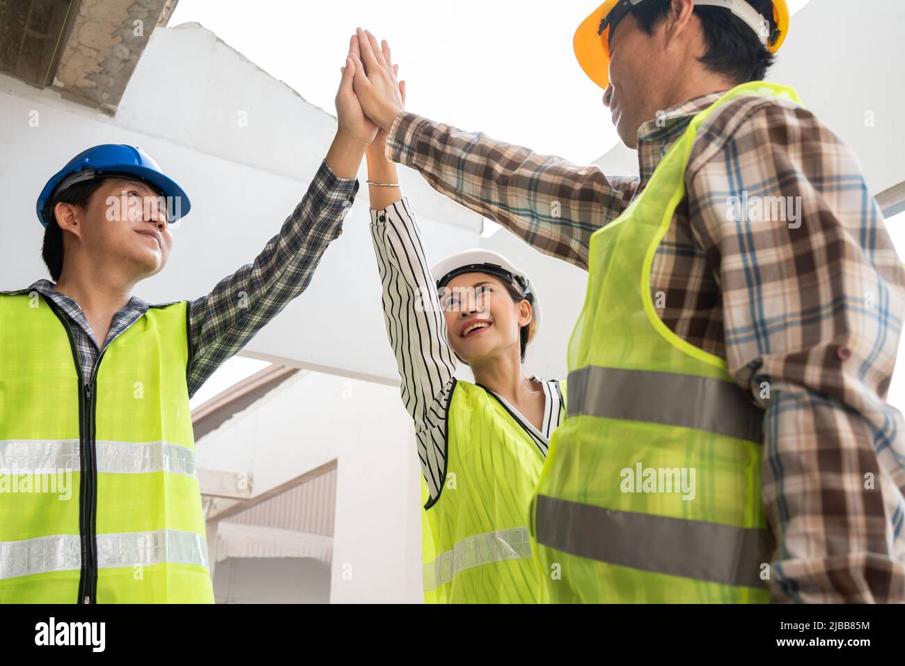 Engineer team and contractor raise their hands up together for joining hands in factory construction building after build success, Concept of success Stock Photo