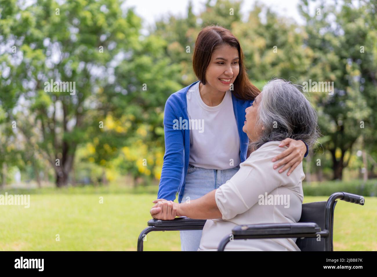 Asian careful caregiver or nurse hold the patient hand and encourage the patient in a wheelchair. Concept of happy retirement with care from a caregiv Stock Photo