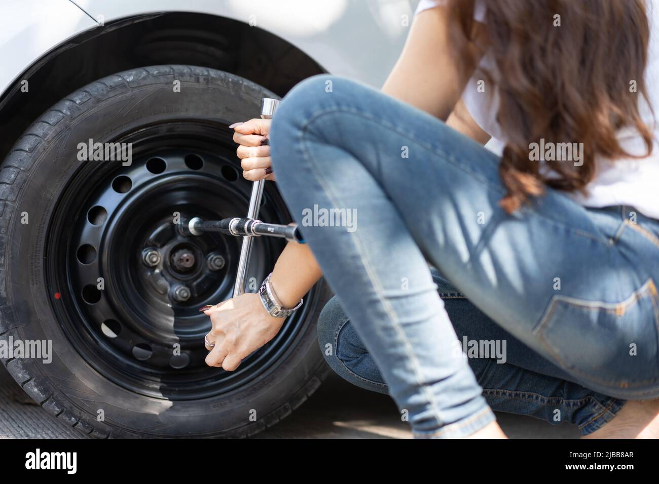 Smart and Attractive Asian woman jacks up her car and uses a wrench to change the wheel on a broken car, uses tools or equipment, tries to solve probl Stock Photo