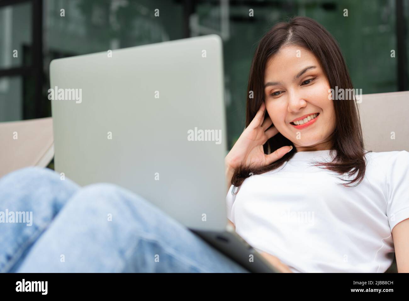 Happy young entrepreneur woman sitting on tanning bed beside pool and using laptop computer for remote online working digital, online business project Stock Photo