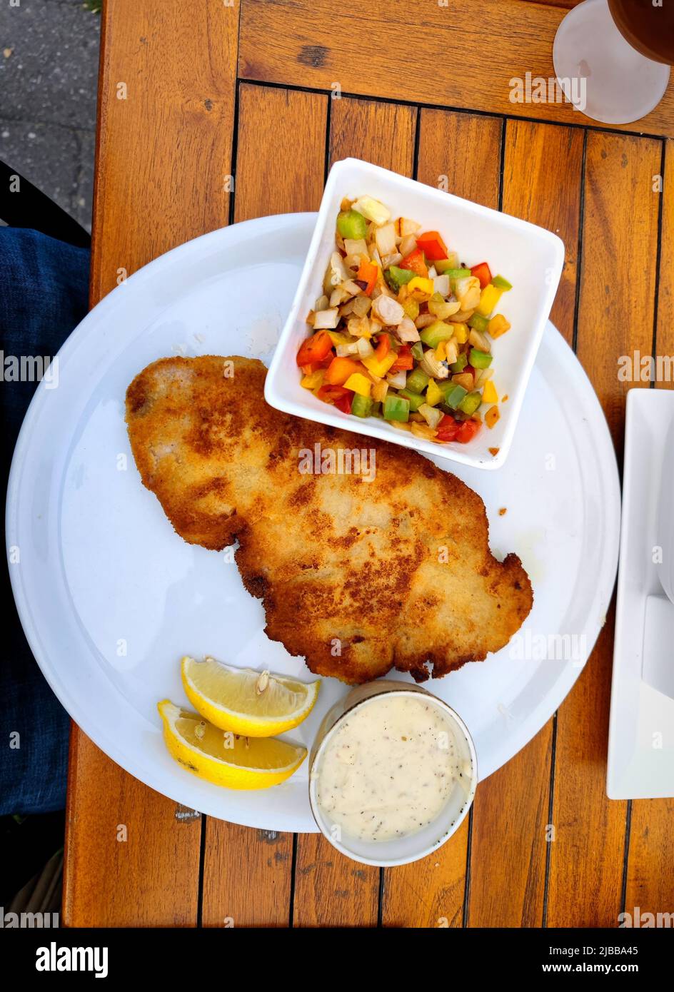 Delicious warm breaded schnitzel with vegetable garnish in a bowl with two sliced lemons next to it and a bowl of hot pepper sauce next to it. Perfect Stock Photo