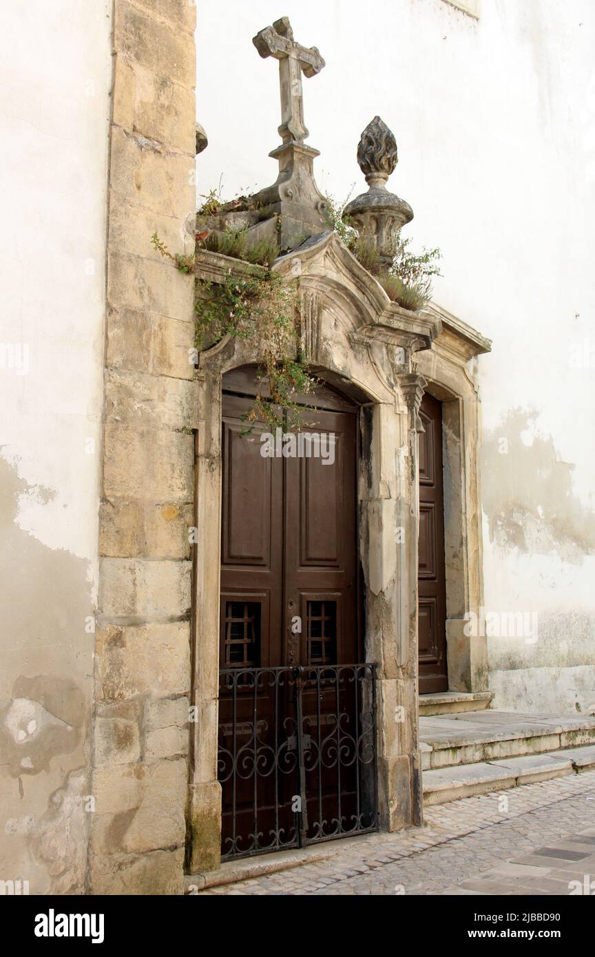 Small chapel with stone-framed wooden door built into an exterior corner of Sao Bartolomeu Church, in the heart of old town, Coimbra, Portugal Stock Photo