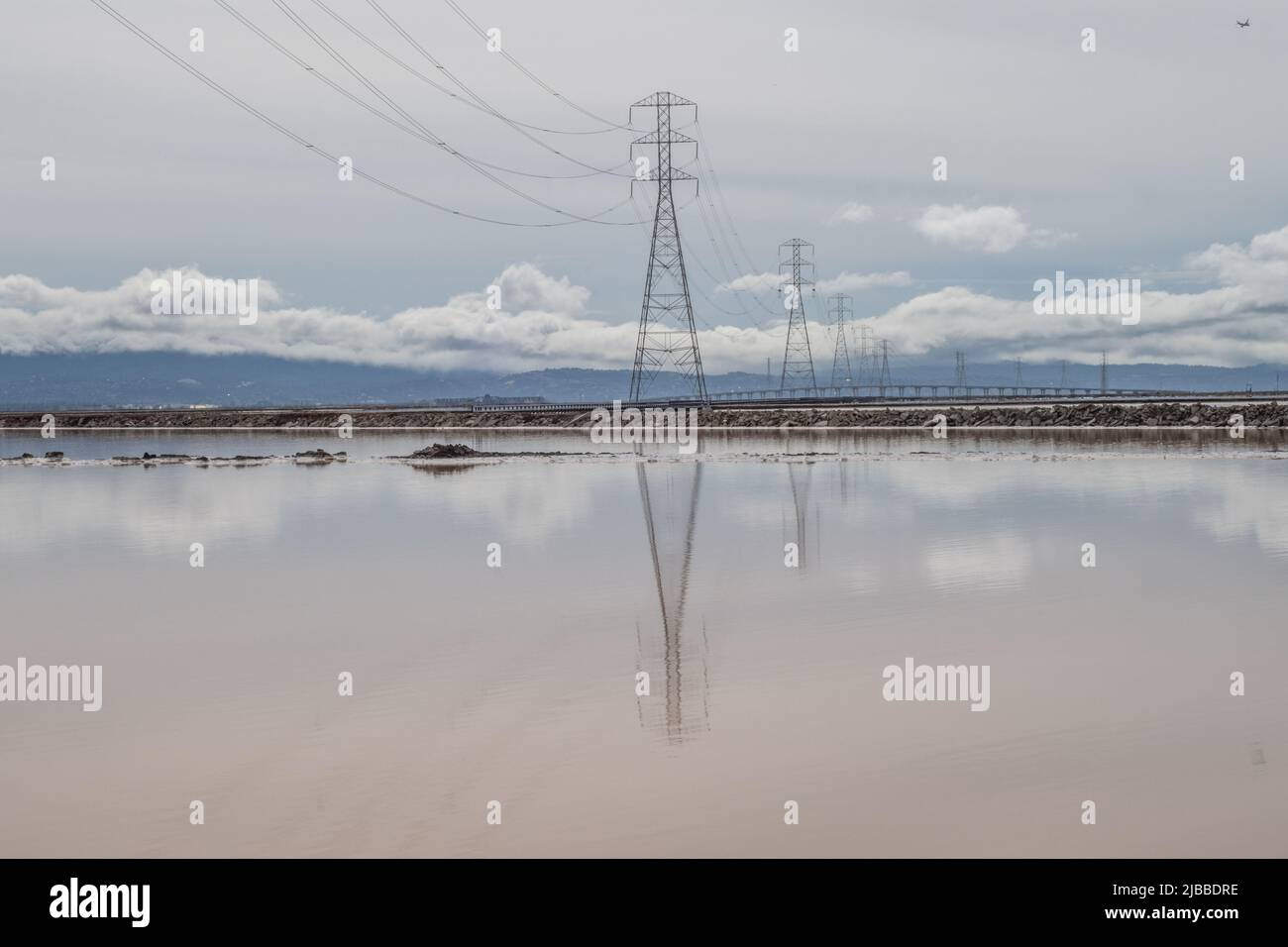 Powerlines stretch over the glass mirrorlike water of salt production ponds Stock Photo
