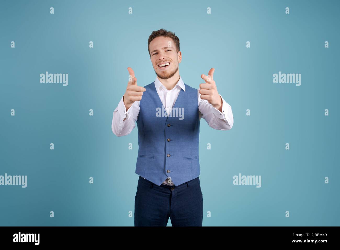 Successful young business in white shirt isolated on blue wall background. Career achievement wealth business concept. Flow out onto a copy of the place. Pointing index finger at the camera Stock Photo