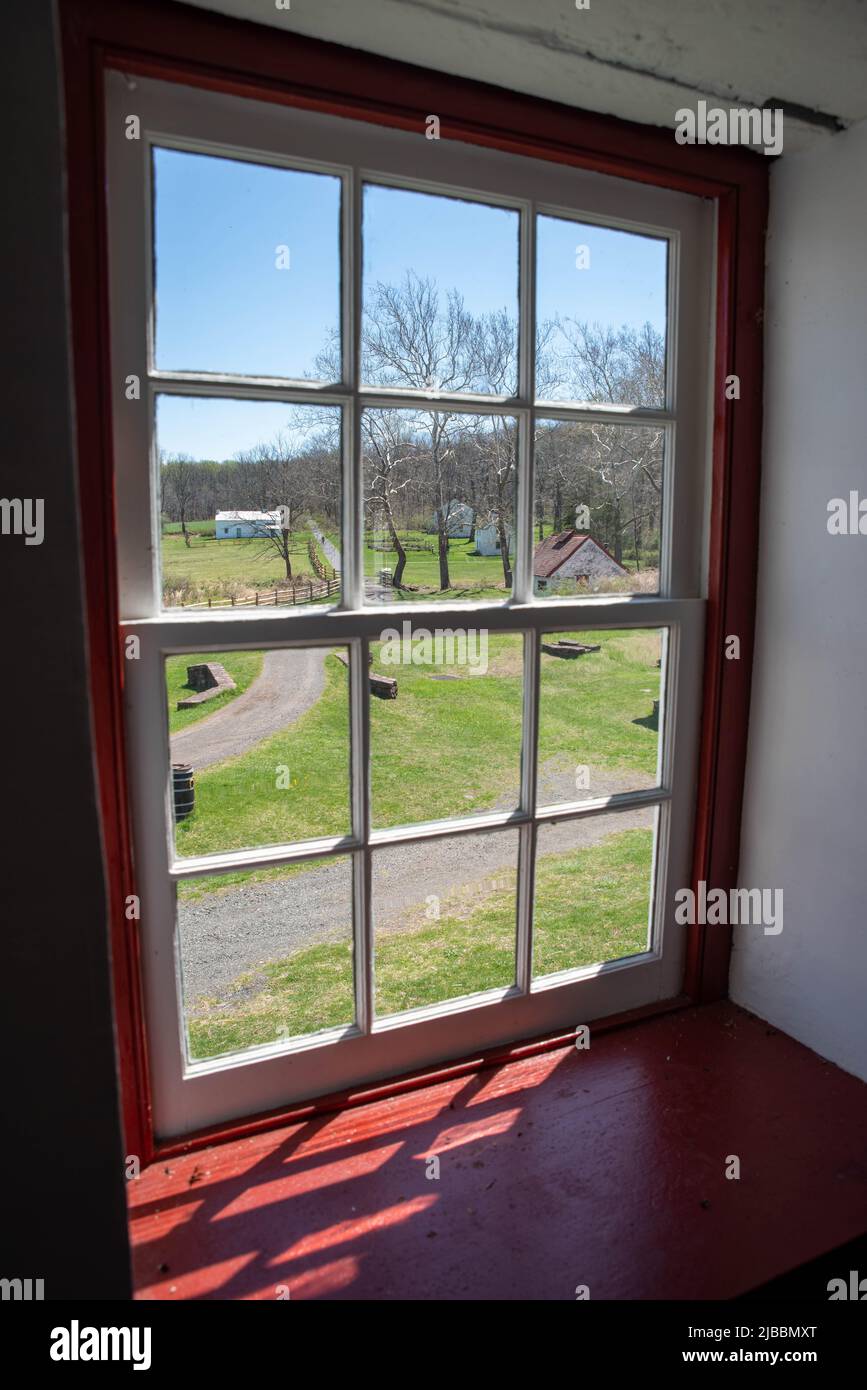 Colonial American rural village lane and buildings seen through an antique red 12-pane Pennsylvania window with sunlight streaming in. Copy space, no Stock Photo