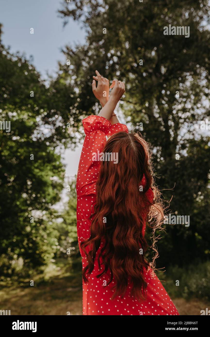 view from the rear back portrait young redhead woman with long hair and reaching out arms to the sky Stock Photo