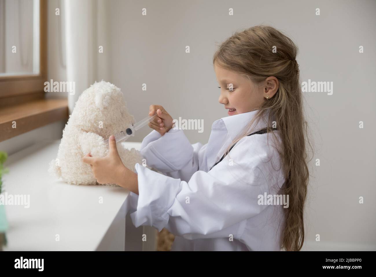 Girl in coat holds syringe makes vaccine to toy bear Stock Photo