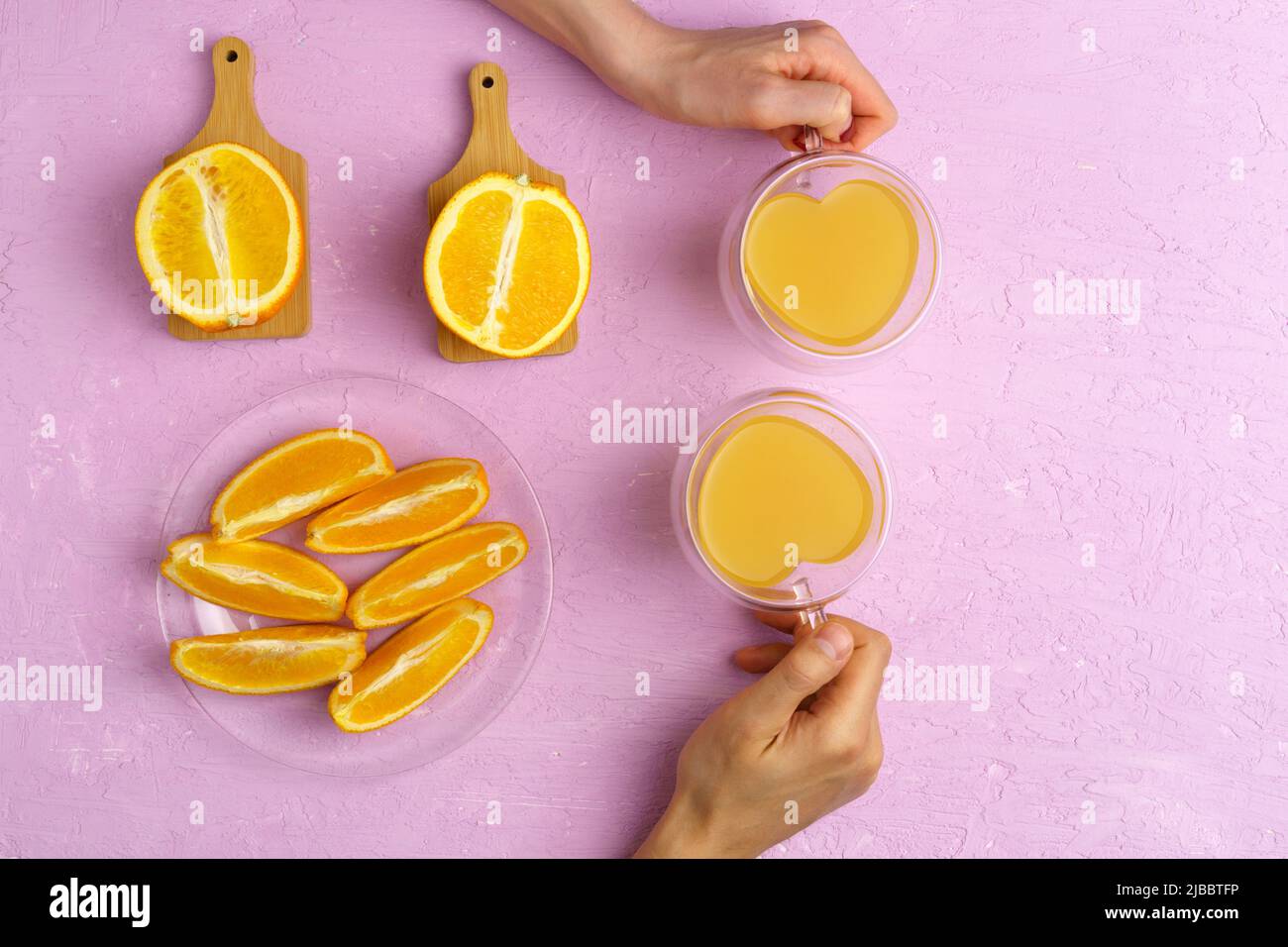Fresh orange juice in glass and oranges on a pink colored background. Top view. Stock Photo