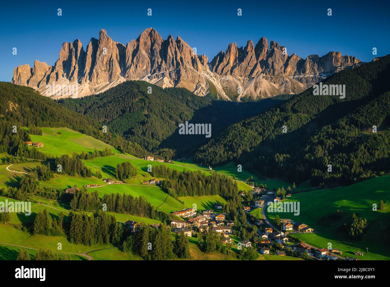 Great view from the hill with summer green fields and high mountains. Beautiful valley with alpine village and pastures on the hills, Santa Maddalena Stock Photo