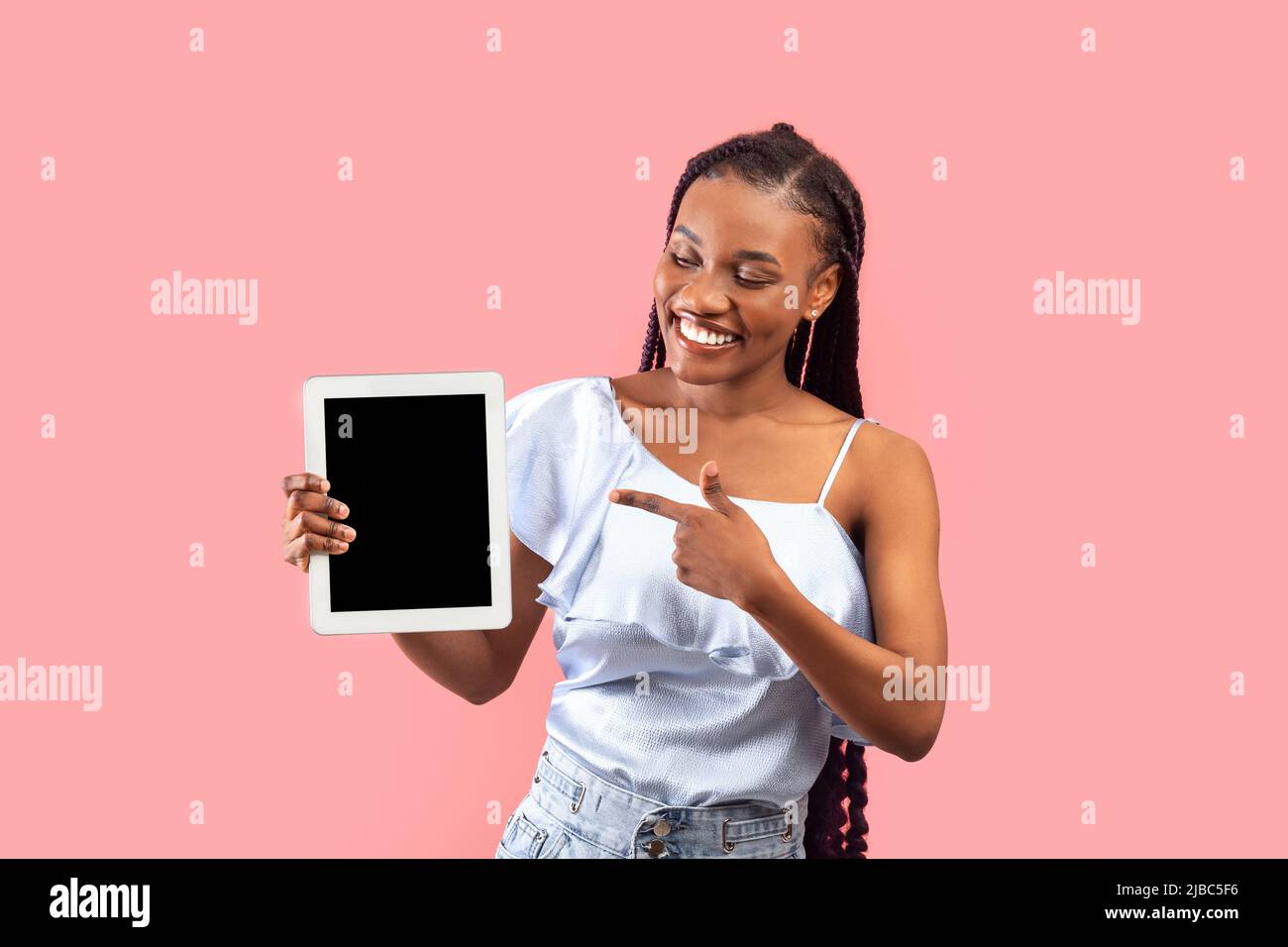 Charming young black woman showing tablet with empty screen on pink ...