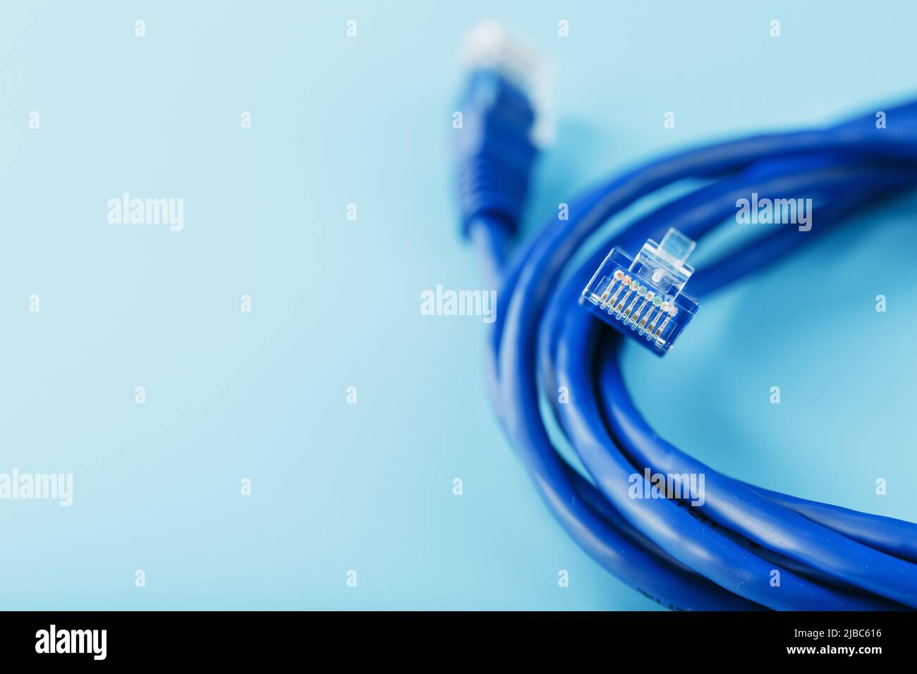 A coil of an Internet network cable for data transmission on a blue background. Patch cord for LAN cable. Stock Photo