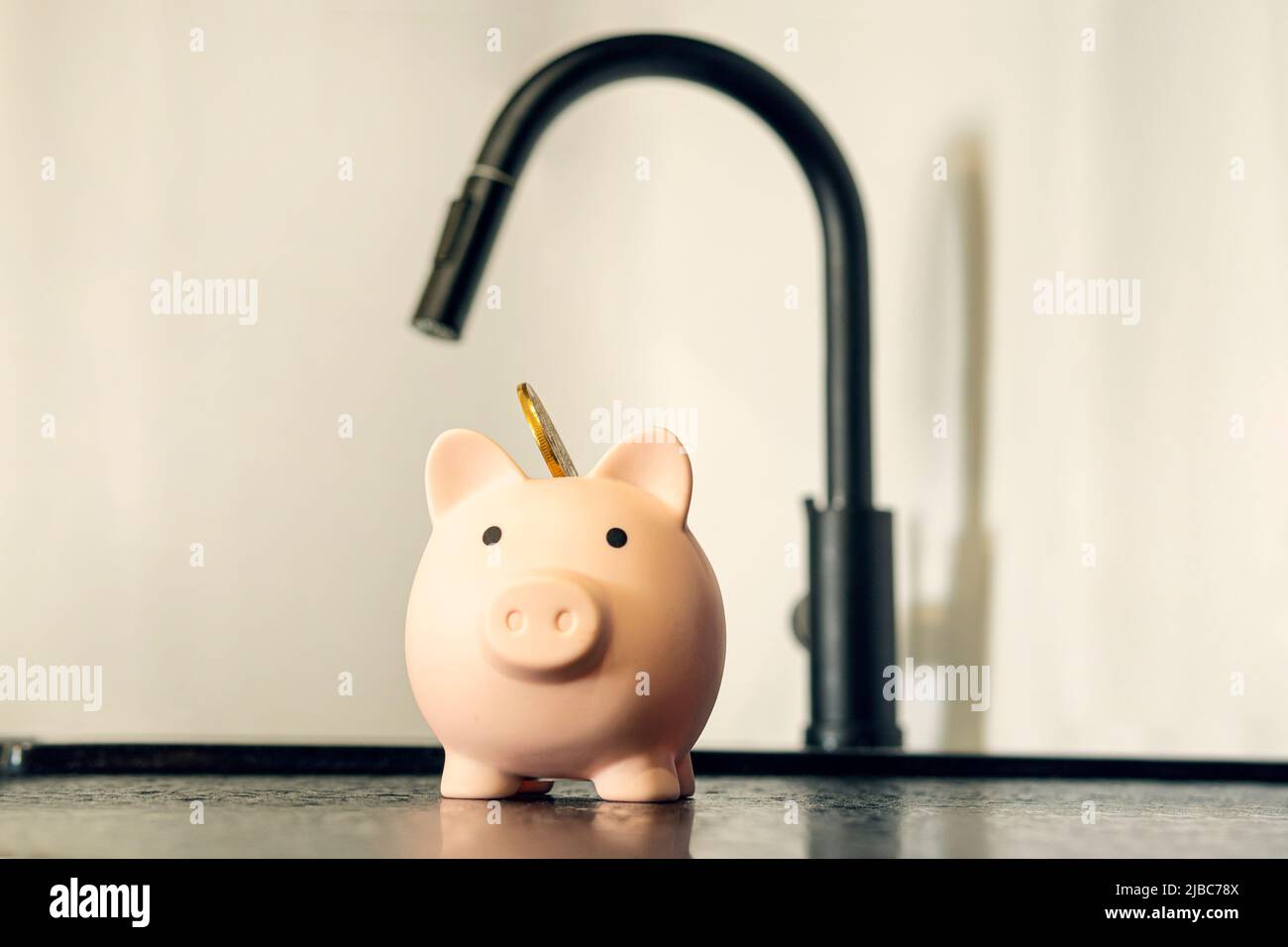Pink piggy bank and tap on wooden surface. Saving water concept the rise in price of housing and communal services. Stock Photo