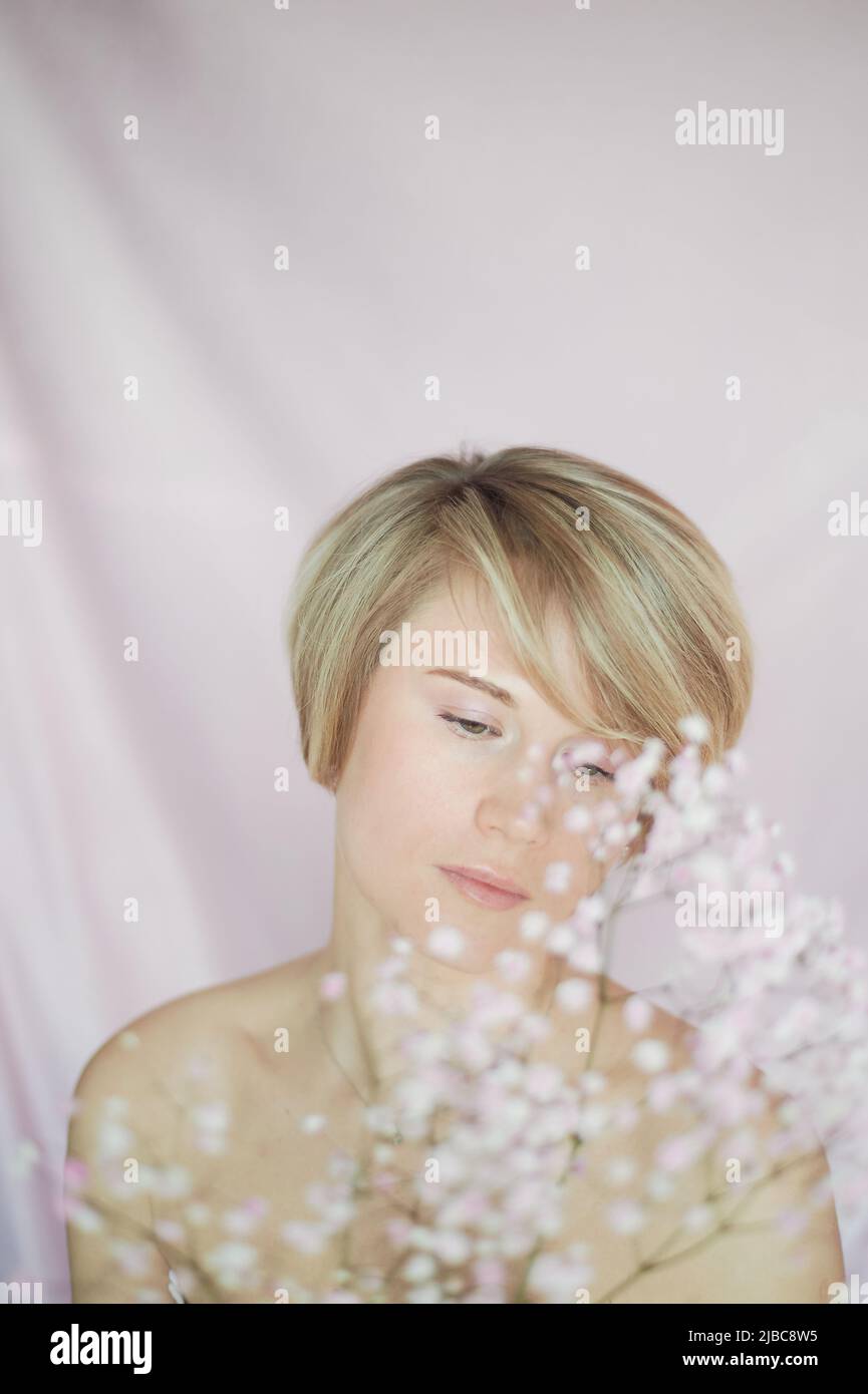 Portrait of a girl on a pink background with flowers. Tenderness and feminine. The sphere of beauty and women's health. Short haircut, blonde hair Stock Photo