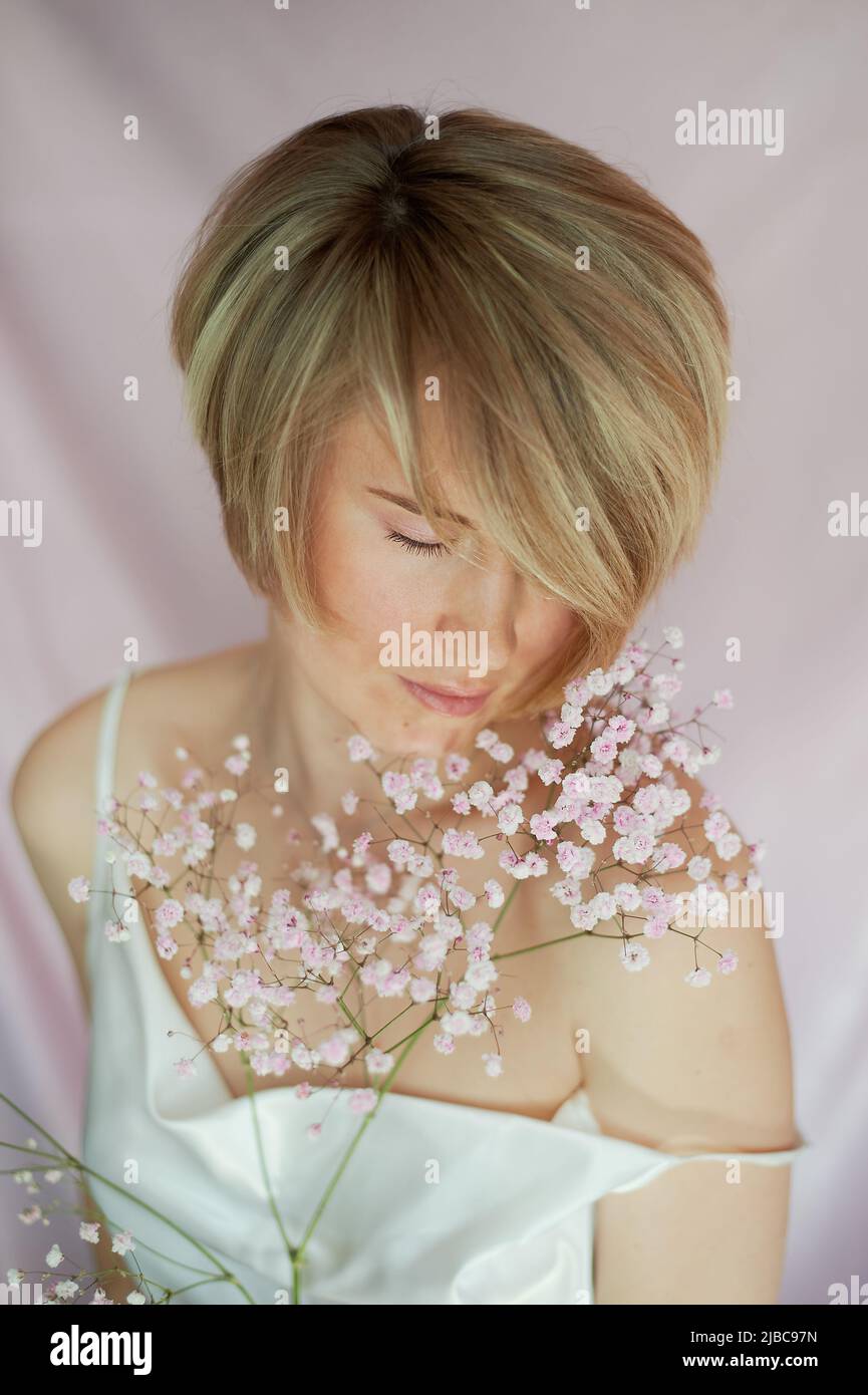 Portrait of a girl on a pink background with flowers. Tenderness and feminine. The sphere of beauty and women's health. Short haircut, blonde hair Stock Photo