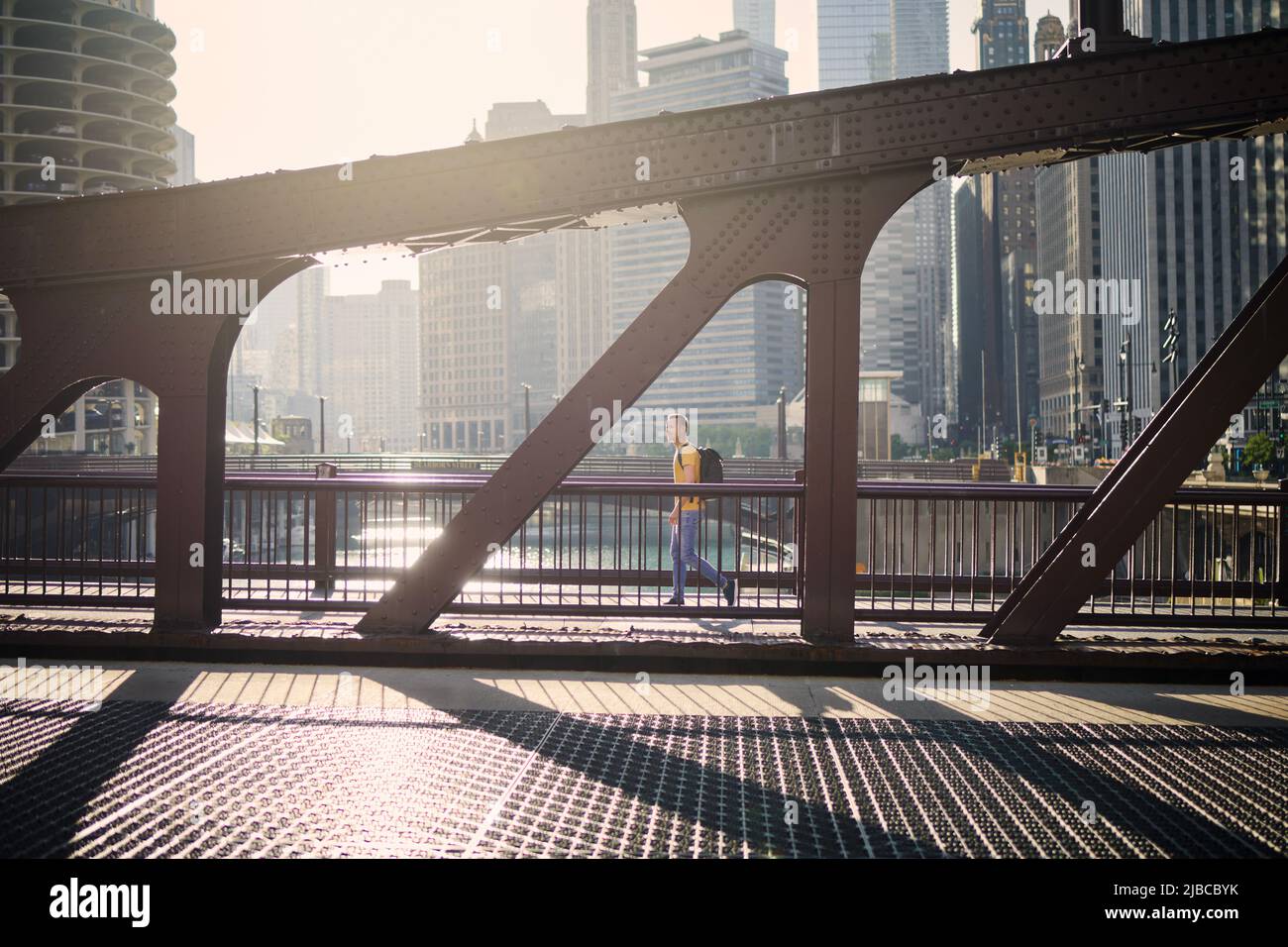 Side view of man on the move while walking on bridge and looking around. City in morning light. Stock Photo