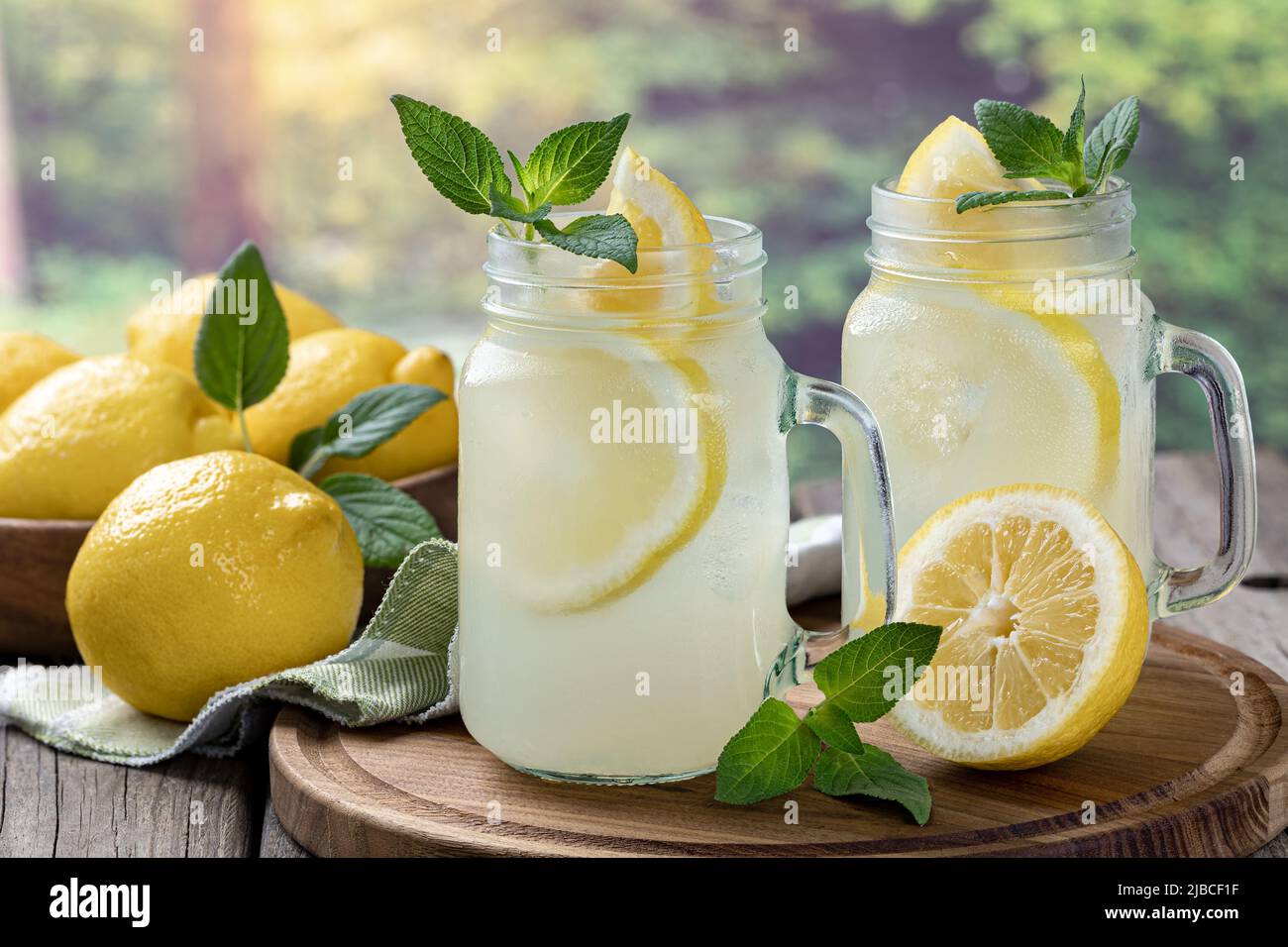 Two glasses of lemonade with mint and lemon on a wooden tray with