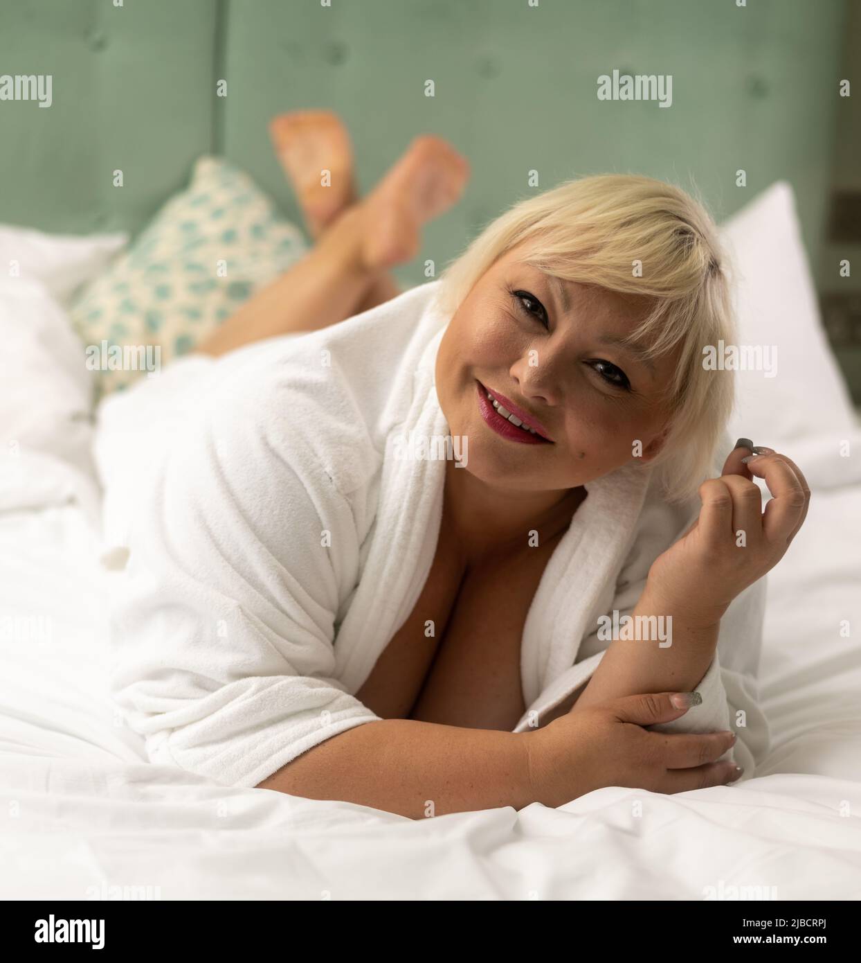 Luxury lifestyle shoot with body positive plus sized female model with white robe on king sized bed Stock Photo