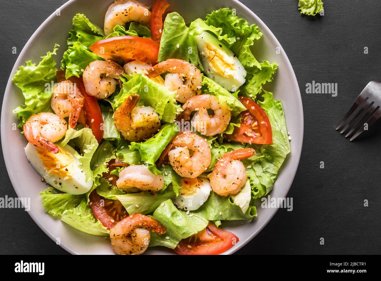 Shrimp Salad. Seafood Caesar Salad on black background, top view, copy space. Stock Photo
