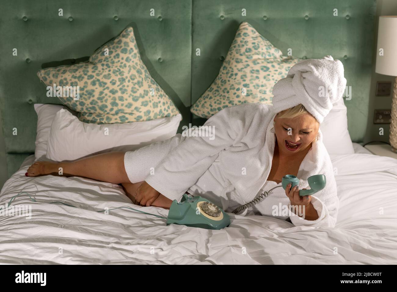 Luxury lifestyle shoot with female model, wearing white robe on king sized bed  with rotary phone, Stock Photo