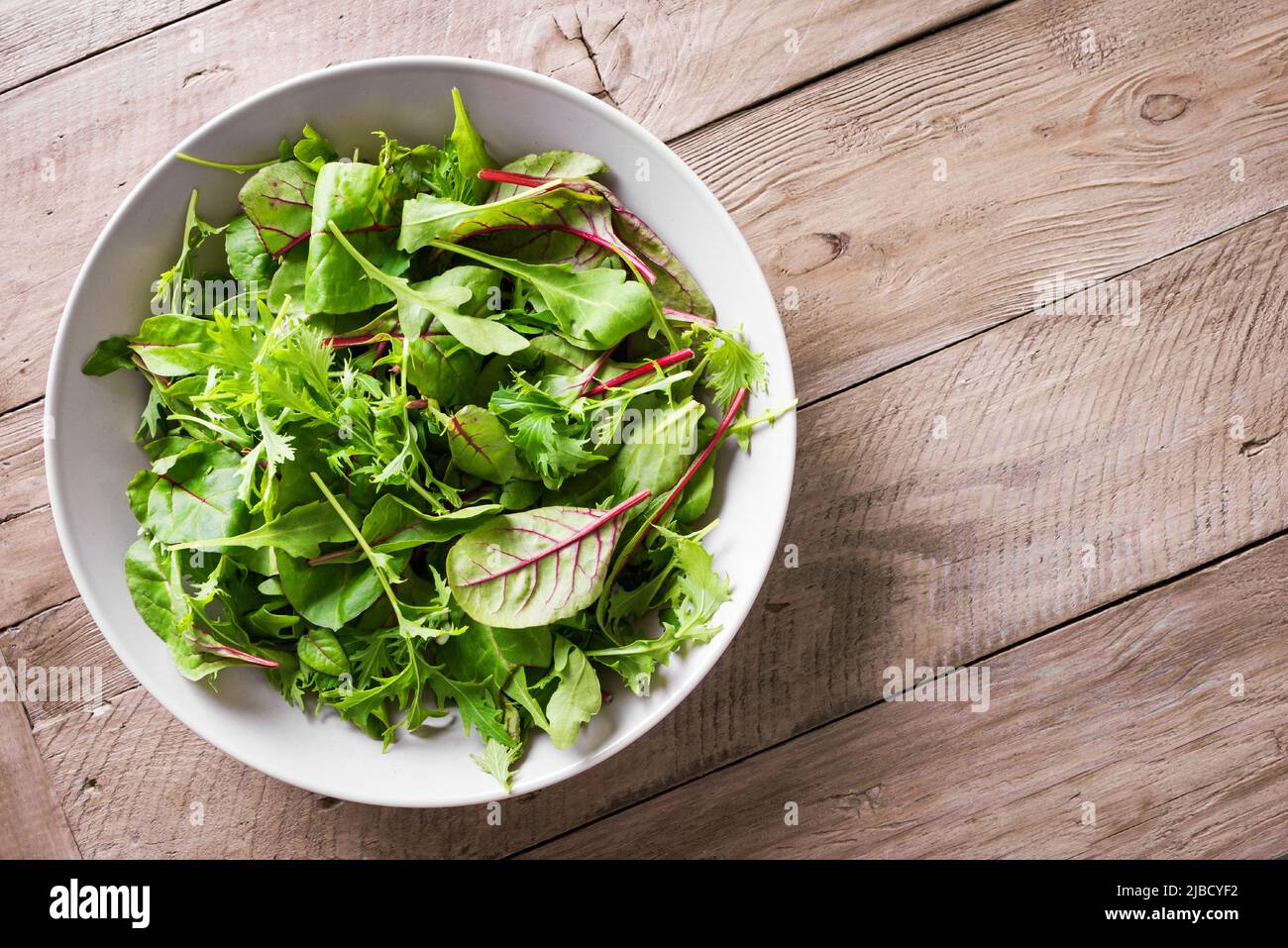 Green Salad Mix. Healthy green salad, fresh organic leaves mix salad with arugula, swiss chard and lettuce, wooden background, top view, copy space. Stock Photo
