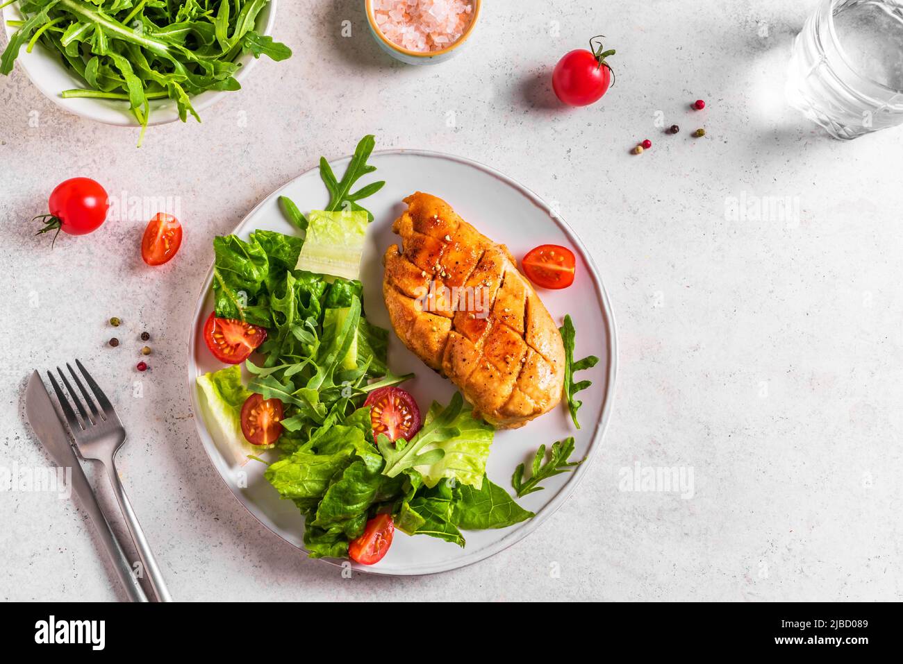 Chicken Salad with fresh vegetables and greens on white table. Roasted Chicken Fillet, green lettuce, arugula, tomatoes salad for healthy lunch. Stock Photo