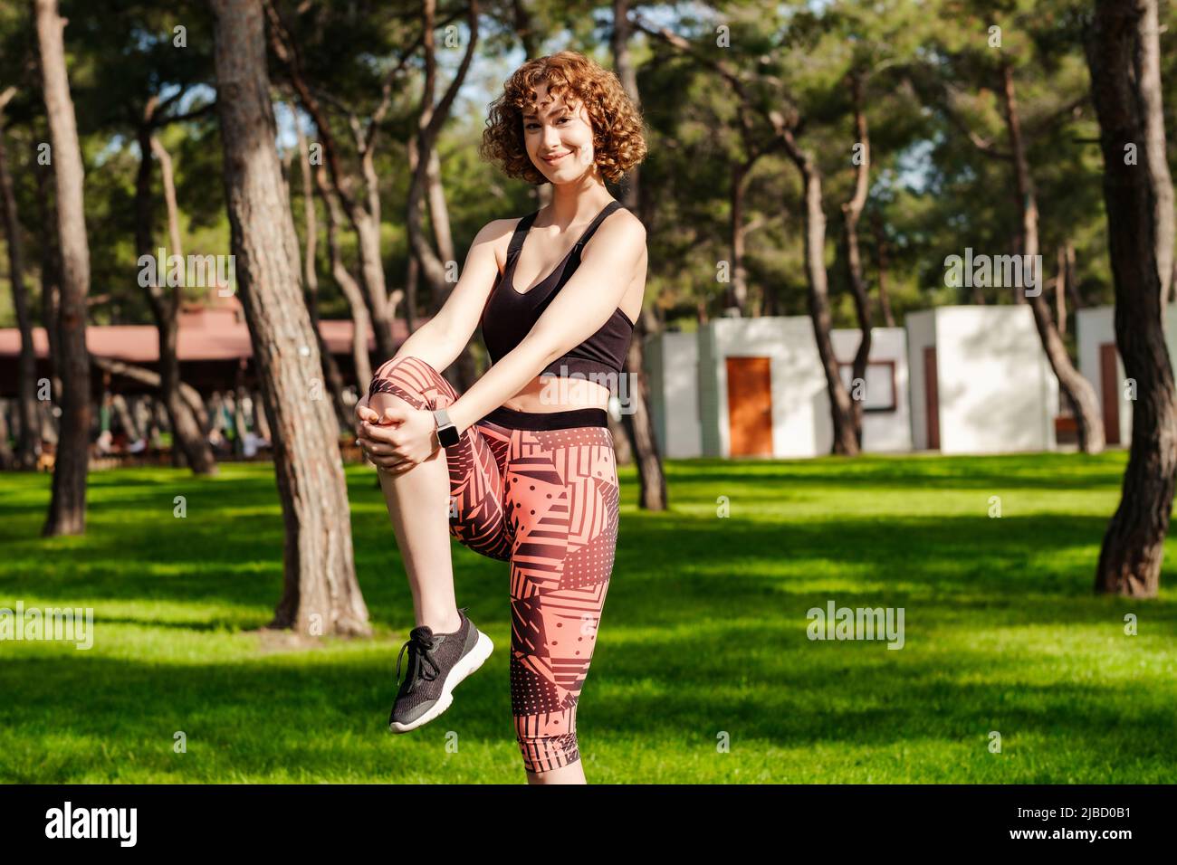 Cheerful redhead woman wearing sports bra standing on city park