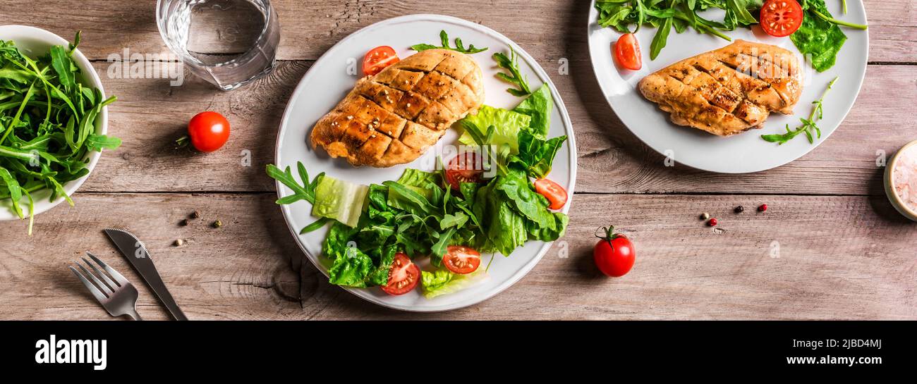 Grilled Chicken Salad with fresh vegetables and greens on wooden table. Roasted Chicken Breast, green lettuce, arugula, tomatoes salad for healthy lun Stock Photo