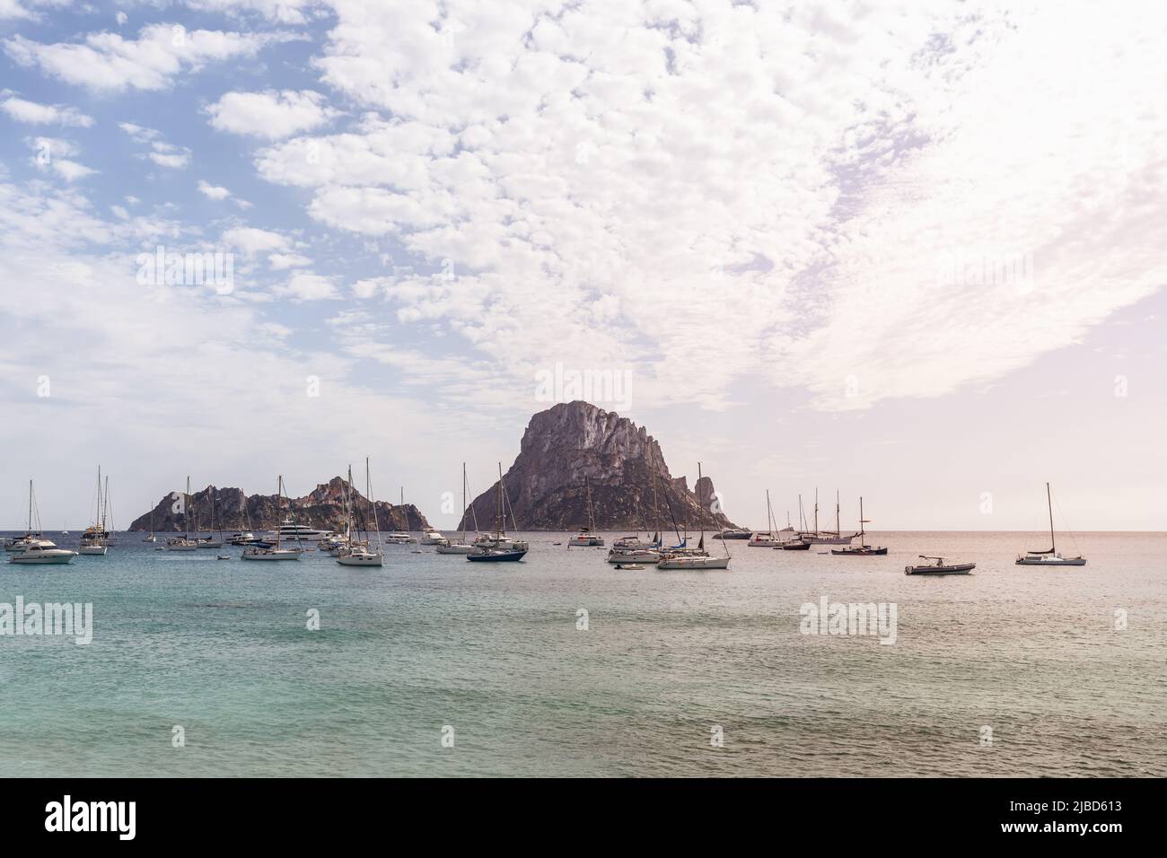 Sailing yachts anchored in Cola d'Hort bay, ripples on water everywhere and two cliff islands Es Vedra and Es Vedranell on horizon, Ibiza Stock Photo