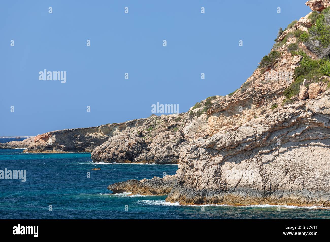 Morning view of the sea and sun-bleached coastal cliffs of Ibiza island under clear, pale blue sky without a single cloud, Balearic Islands, Spain Stock Photo