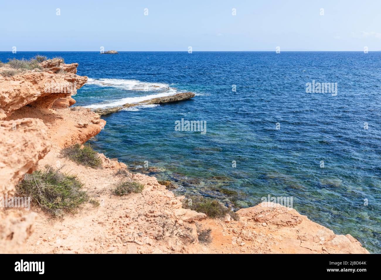 Orange-pink rocky coast with rare plants, water changes color depending on depth, clear sky, summer day, Ibiza, Balearic Islands, Spain Stock Photo
