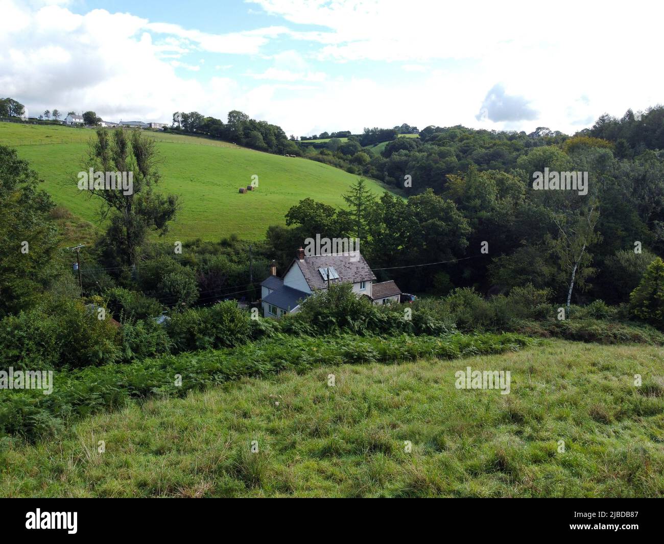 A Devon farmhouse enstles in a valley between fields Stock Photo
