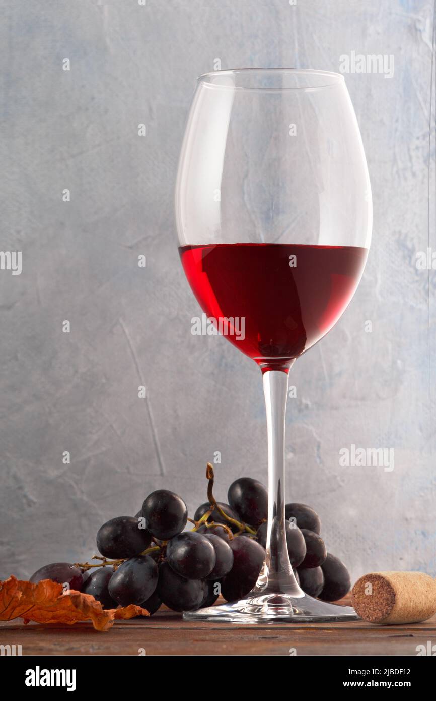 A glass of red wine with grapes and cork on a wooden table. Close-up Stock Photo