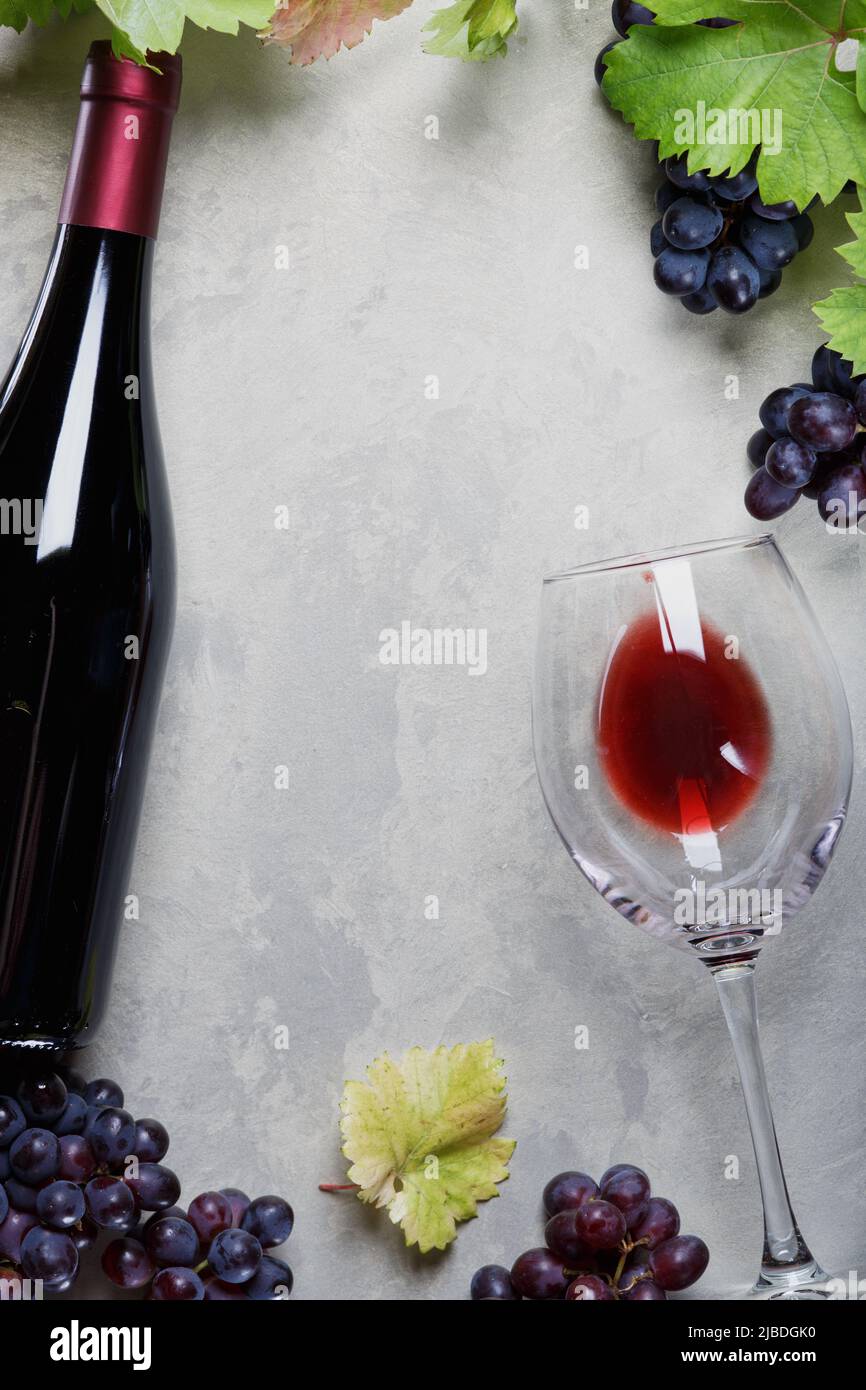 A glass of red wine and a bottle of grapes and grape leaves on the ...