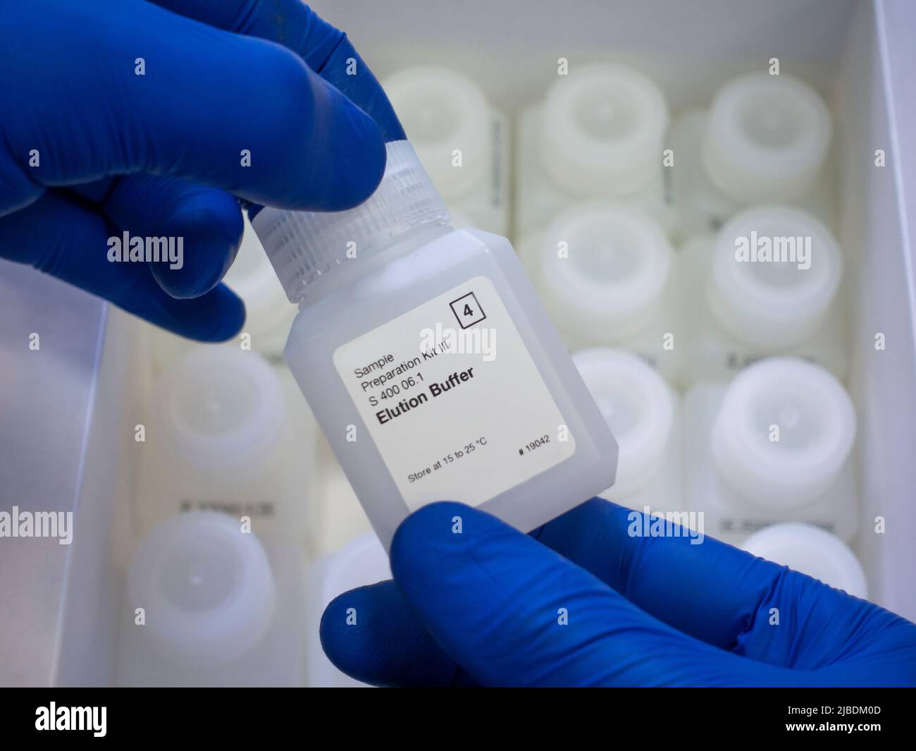 Close-up, two hands in blue gloves hold a white chemical reagent bottle, assay buffer, reagent kit from the box Stock Photo