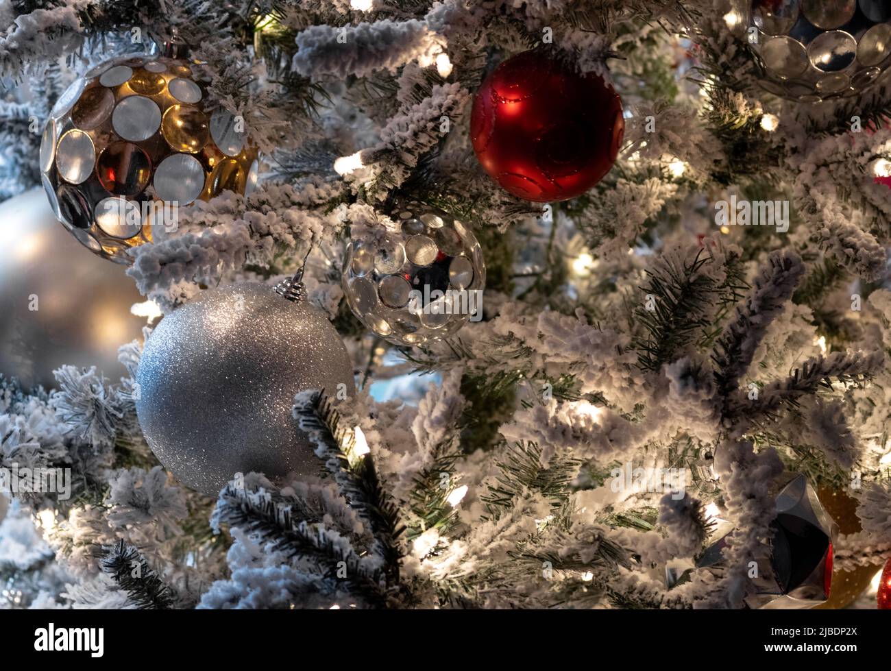 close up christmas decoration scene, white lights on snow covered tree with red and white, silver and gold christmas balls, festive holiday scene Stock Photo
