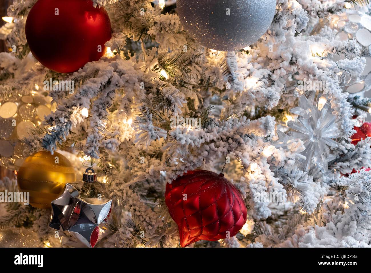 warm lighting, close up christmas decoration scene, white lights on snow covered tree with red, white, silver and gold christmas balls, festive holida Stock Photo