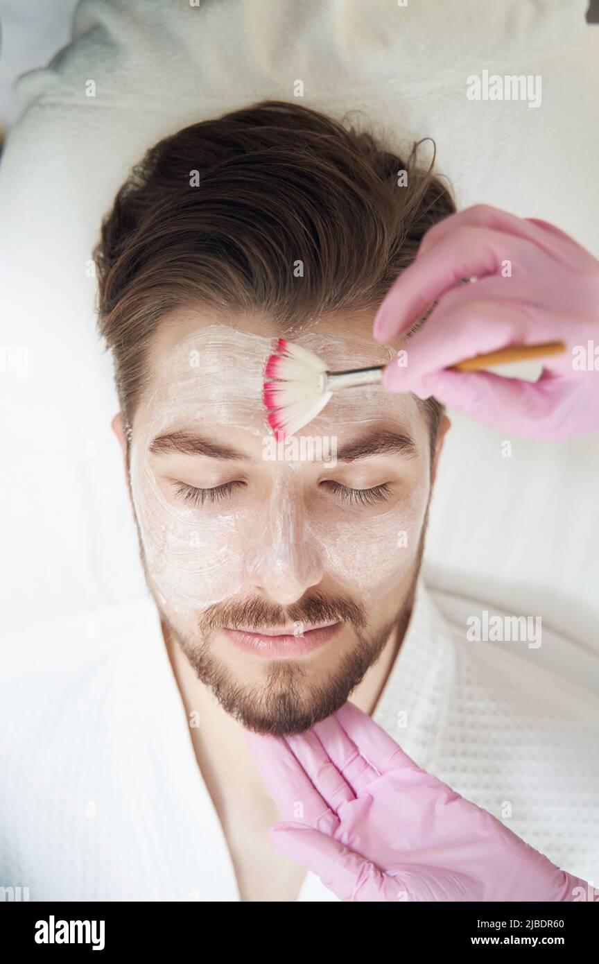 Beautician supporting man chin while spreading cream on forehead Stock Photo
