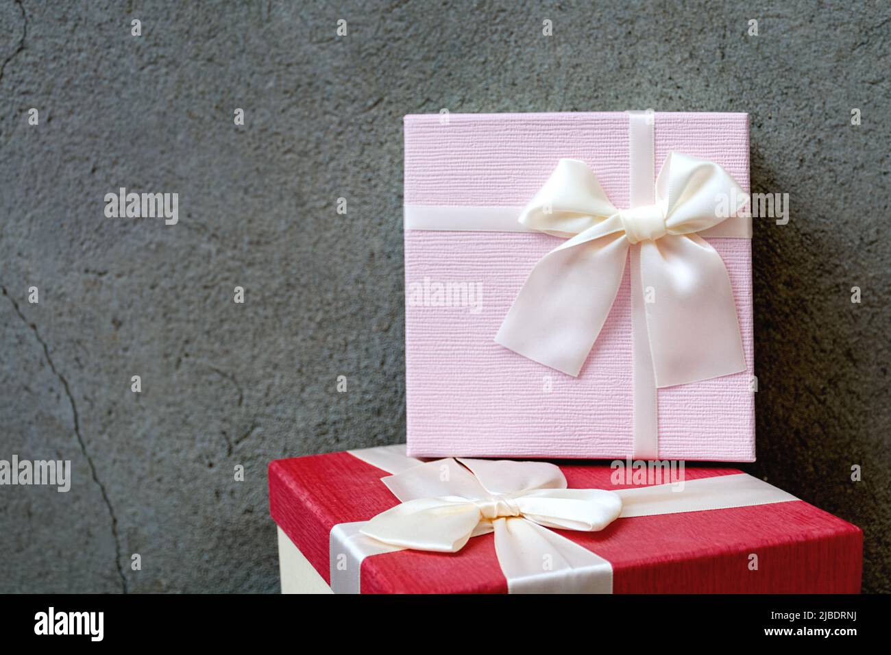 Front view of two beautiful gift boxes with satin ribbon on a background of natural concrete wall. Pink and red gift for Father's Day or Christmas. Copy space for text Stock Photo