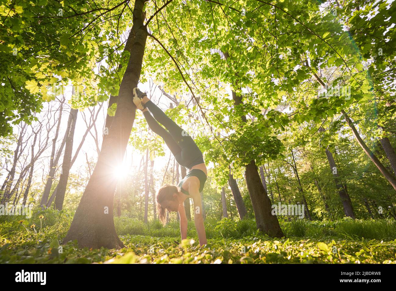 Athletic slim woman exercising balance in handstand in nature Stock