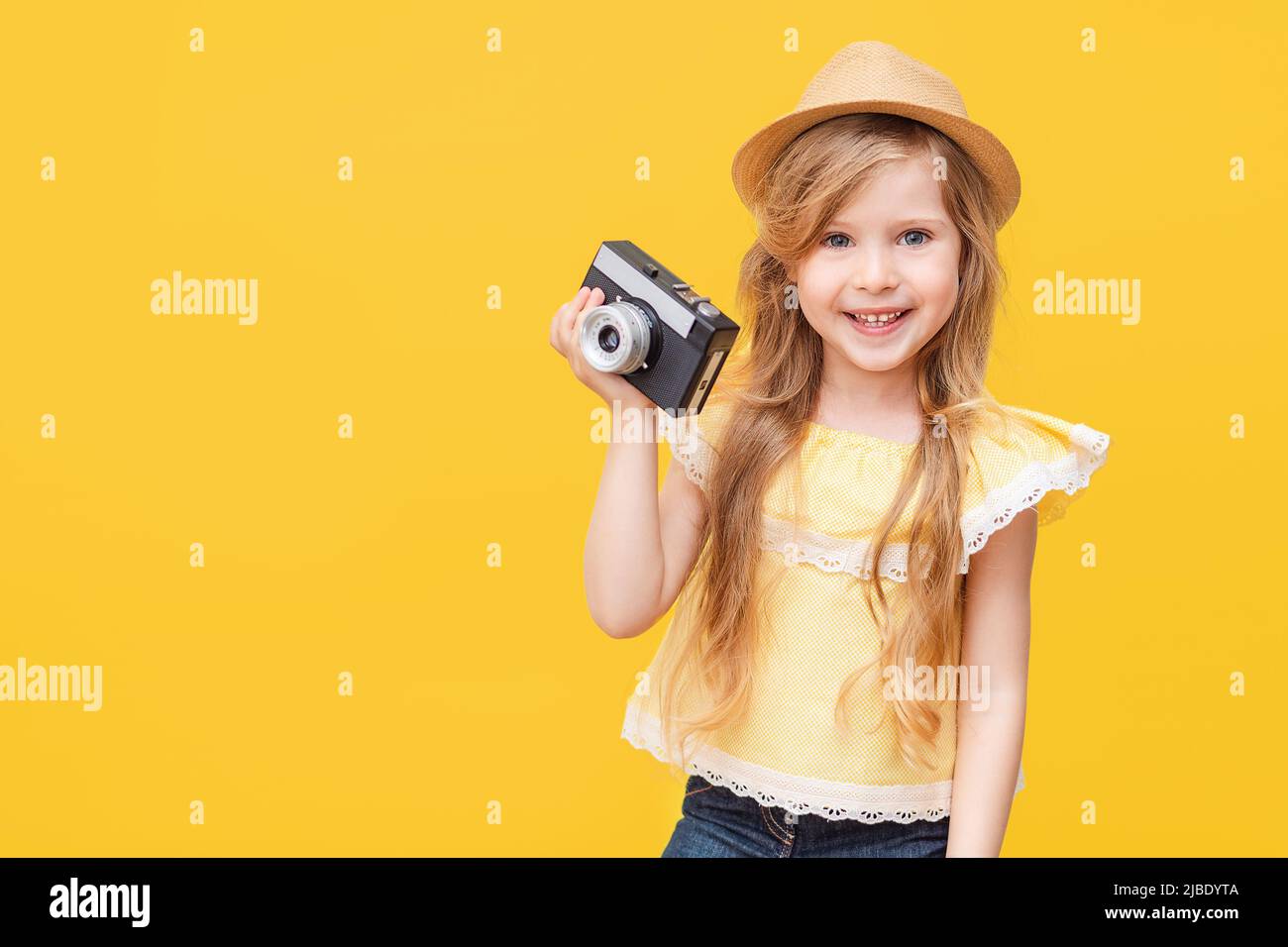 Portrait of a happy child a little blonde girl with long hair on a Colored yellow background with a retro camera in her hands. The concept of rest Stock Photo