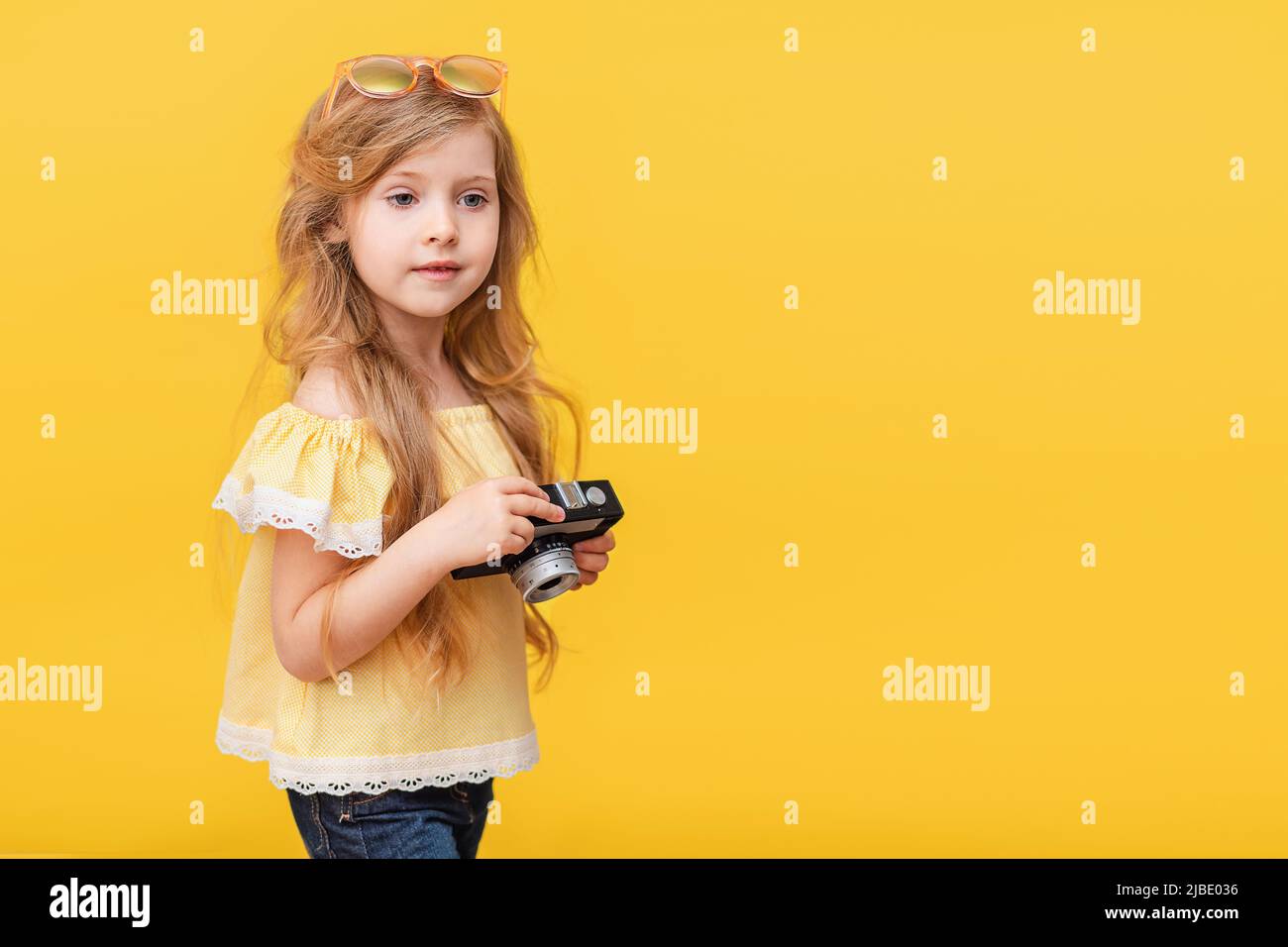 Portrait of a happy child a little blonde girl with long hair on a Colored yellow background with a retro camera in her hands. The concept of rest Stock Photo
