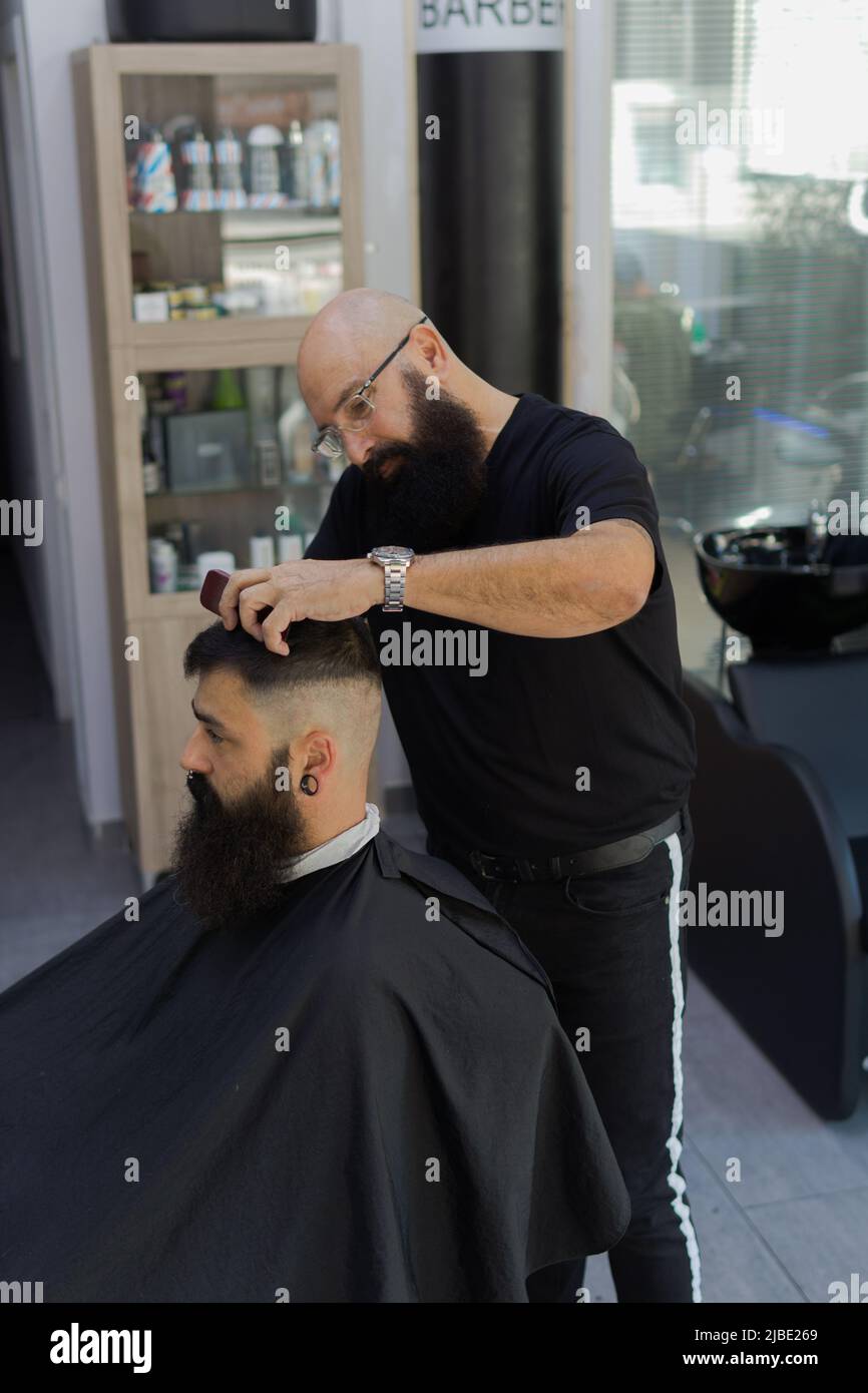 Barber doing haircut to a bearded man inside barber shop in the morning