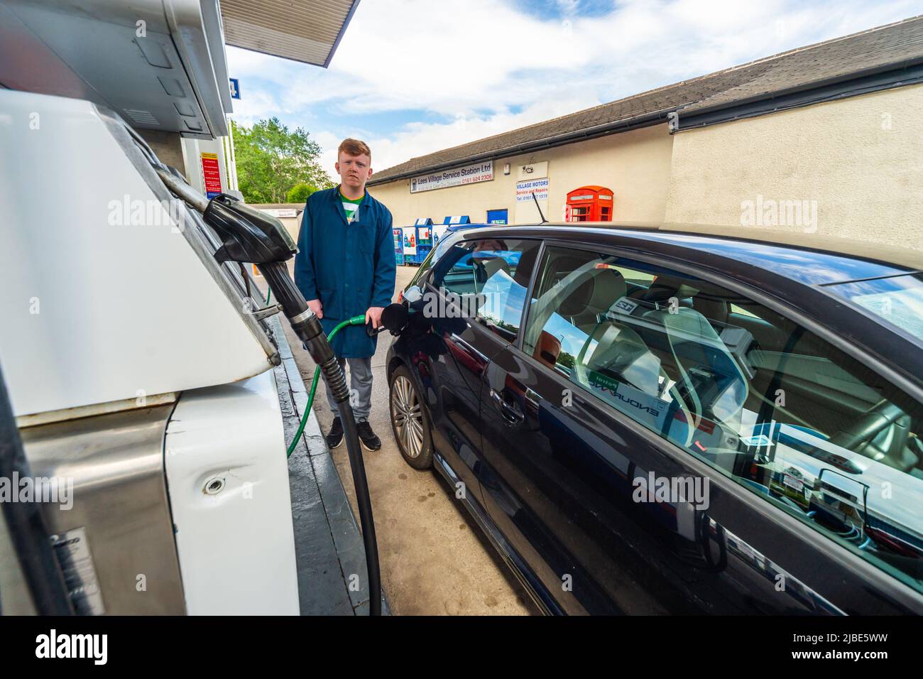 Filling station attendant dispensing unleaded fuel into a car on the forecourt. Wide view. Attendant service is rare in the UK nowadays Stock Photo