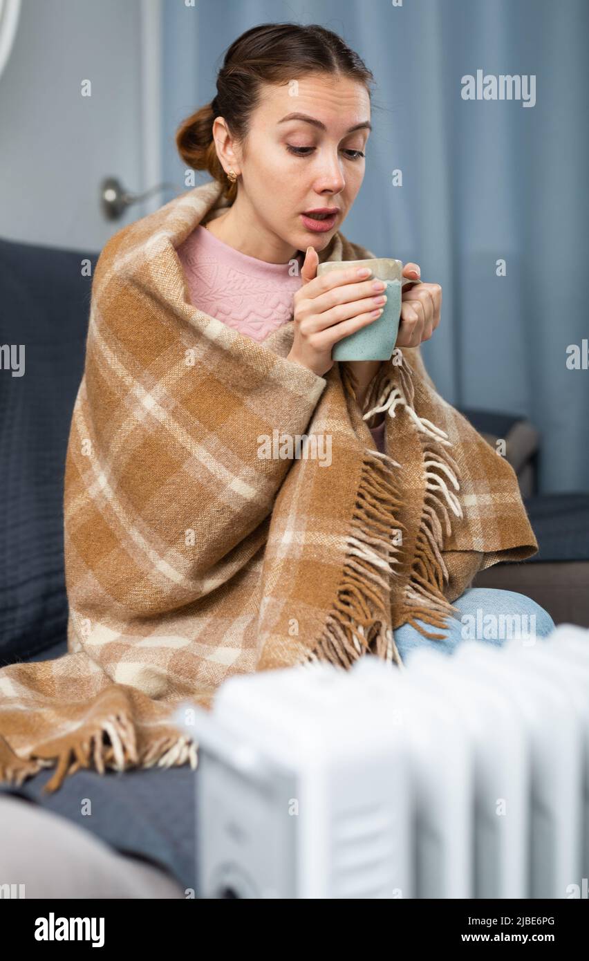 Adult woman with cup near heater in home closeup Stock Photo