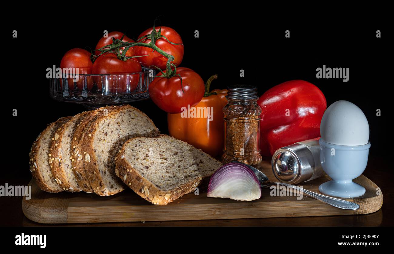 On the kitchen board, a set of healthy breakfast with coarse bread. Red tomato mares, red and yellow peppers, a boiled egg, a salt and pepper shaker. Stock Photo