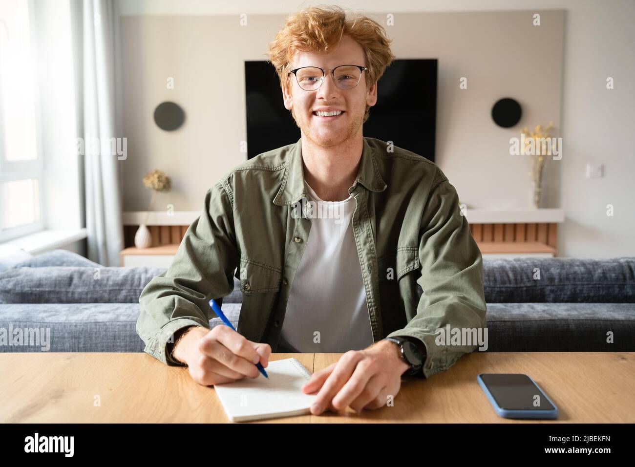 Young man writing notes looking at camera holding videoconference webcam view Stock Photo